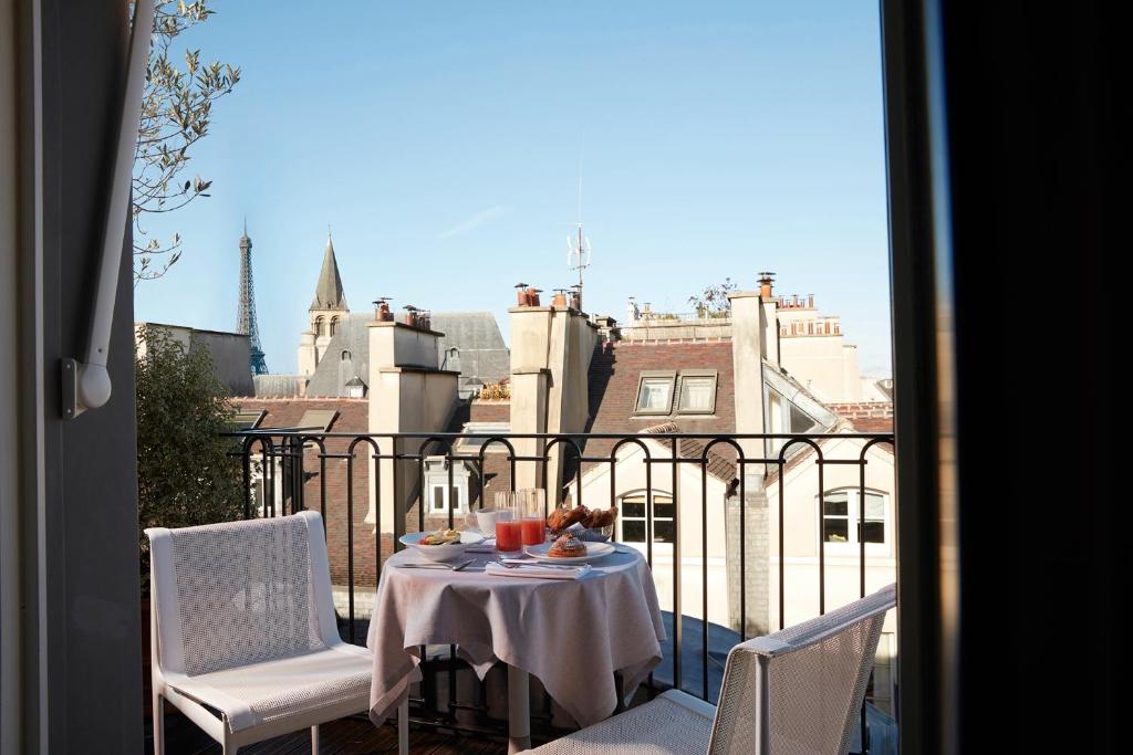 13 Unique Hotels in Paris for a Stylish Stay 57 Breakfast table with two chairs on a balcony at one of the unique hotels in Paris, overlooking charming rooftops, with the Eiffel Tower and a church spire visible in the distance under a clear blue sky.