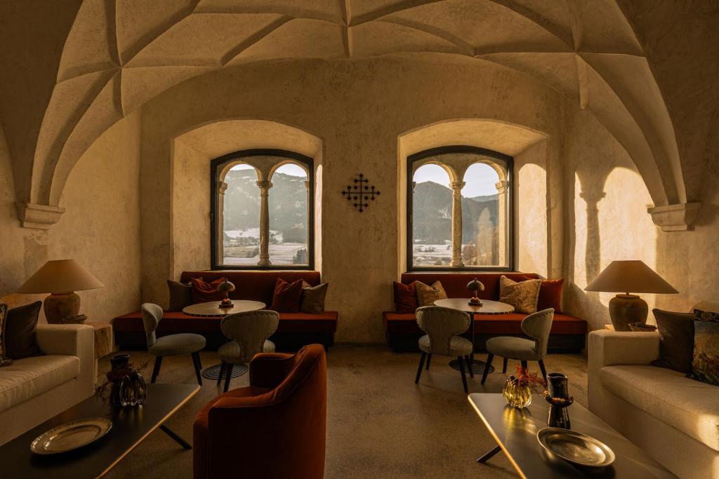 A cozy, sunlit lounge in one of the best hotels in the Dolomites, featuring arched ceilings, plush seating, round tables, and large windows with stunning mountain views. Warm tones and soft lighting create an inviting atmosphere.