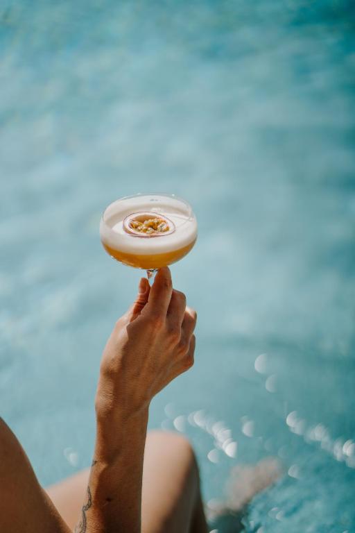 A hand holding a cocktail with a frothy top, garnished with passion fruit, against a blurred blue swimming pool background—perfect for relaxing at one of the best hotels in the Dolomites.