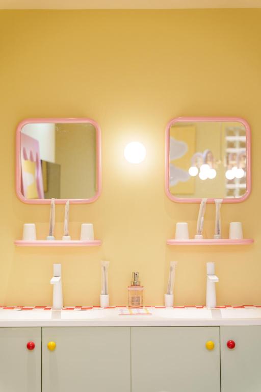 15 Unique Hotels in Tokyo: Coolest hotels 61 A brightly lit bathroom in one of the unique hotels in Tokyo features pastel yellow walls, two pink-framed mirrors, white sinks, toothbrushes in cups, and a soap dispenser on a white countertop with colorful cabinet knobs.