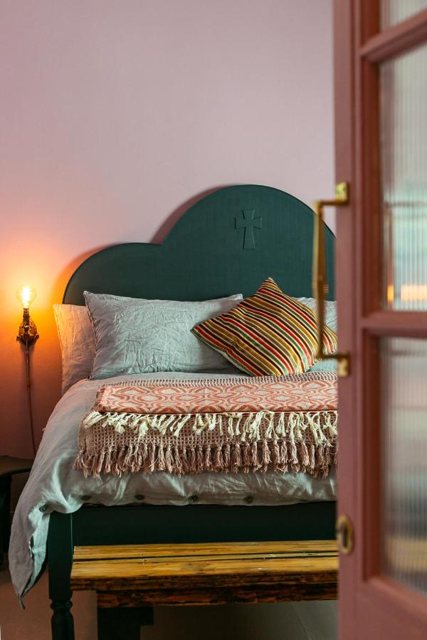 Unique Places to Stay in Cape Town 19 A cozy bedroom with a dark green bed frame, light bedding, a striped cushion, and a pink throw blanket welcomes you through a partially open pink door—one of the unique places to stay in Cape Town.