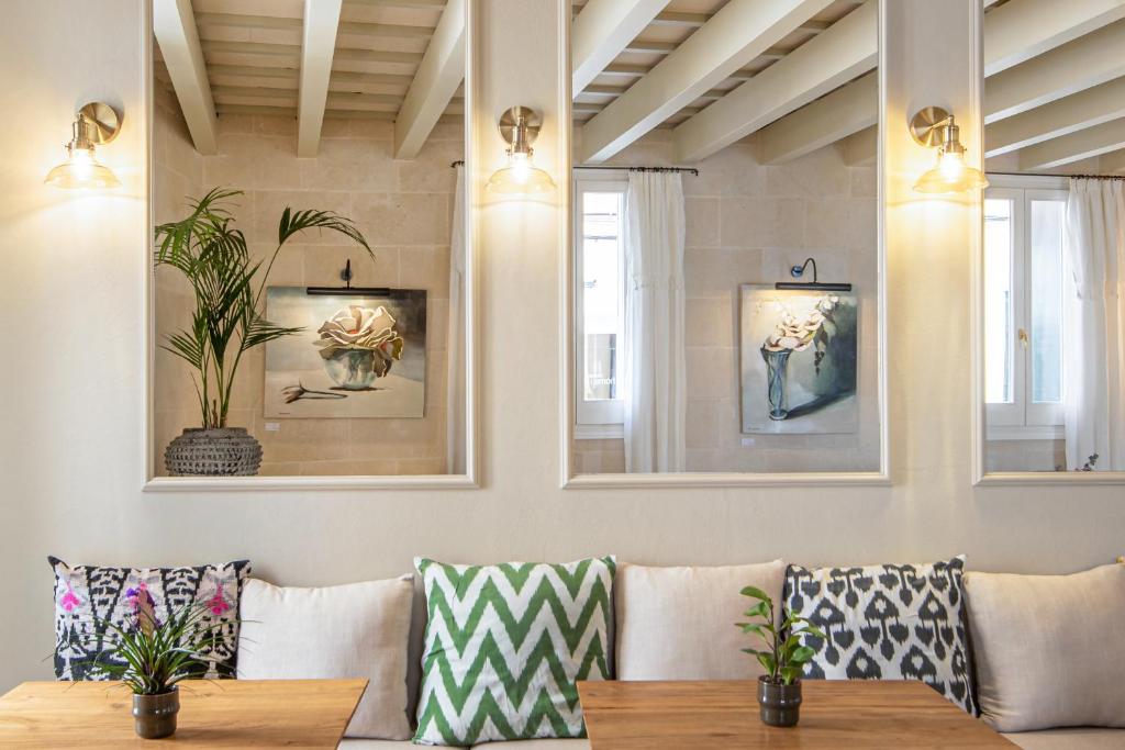 Unique Boutique Hotels in Menorca 49 A cozy seating area with patterned cushions, wooden tables, potted plants, wall art, and large mirrors reflecting the light from wall sconces—just like the inviting lounges found in boutique hotels in Menorca. Cream walls and exposed beams complete the look.