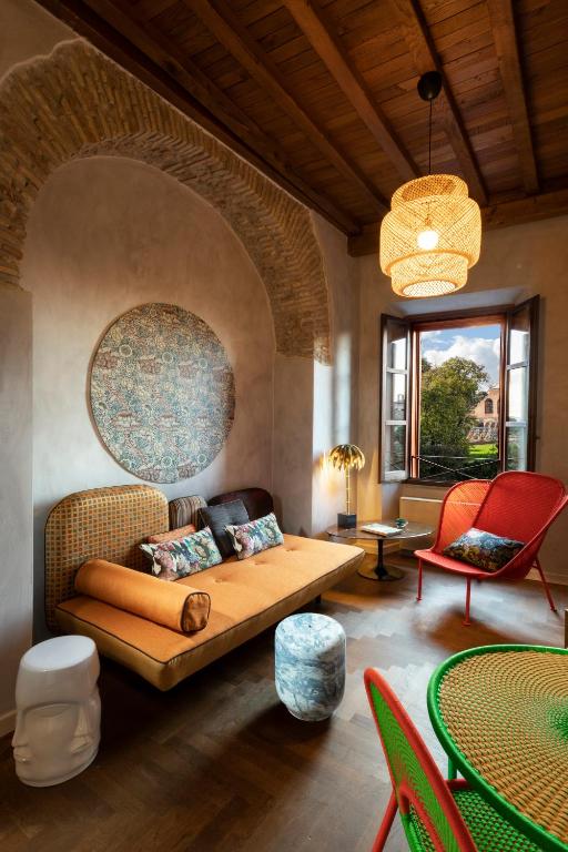 13 UNIQUE Boutique Hotels in Rome 37 Cozy living room with a wooden ceiling, arched stone wall, orange sofa, patterned pillows, red chairs, round wall art, wicker pendant lamp, colorful table—reminiscent of the charming interiors found in boutique hotels in Rome.