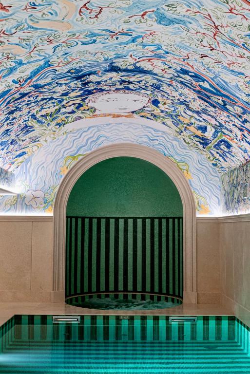 13 Unique Hotels in Paris for a Stylish Stay 39 A small indoor pool with striped green tiles, an arched entry, and a ceiling decorated with colorful abstract patterns awaits at one of the unique hotels in Paris. Neutral stone walls add elegance to this vibrant retreat.