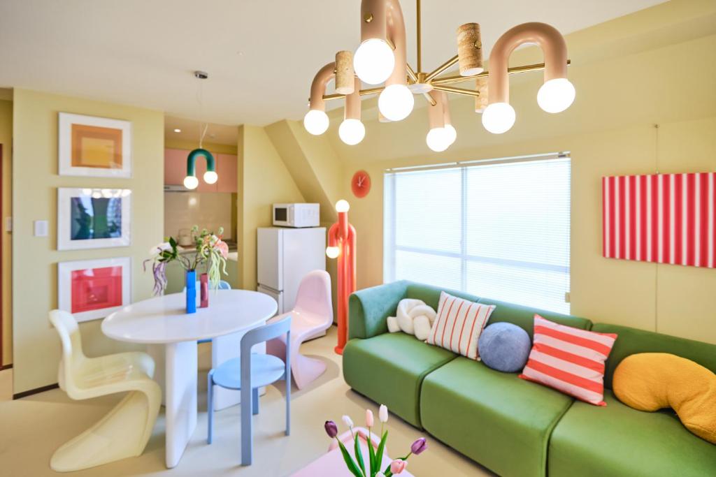15 Unique Hotels in Tokyo: Coolest hotels 59 A brightly lit, colorful living room inspired by unique hotels in Tokyo, featuring a green sofa, assorted striped and round pillows, a white dining table with mismatched chairs, modern lighting, wall art, and a large window with blinds.