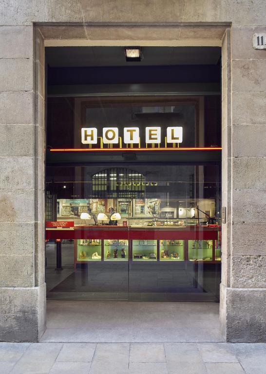 13 Unique Hotels in Barcelona, Spain 31 A hotel entrance with large illuminated HOTEL letters above a glass door welcomes you. Through the glass, the lobby and reception area are visible. The stone facade adds charm, making it one of the unique hotels in Barcelona.