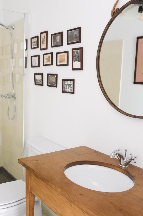 Top 12 Boutique Hotels in Porto, Portugal 47 A bathroom with a wooden vanity and round mirror, white sink, toilet, and a glass-enclosed shower—echoing the chic style of boutique hotels in Porto. Several small framed pictures are arranged on the white wall above the toilet.