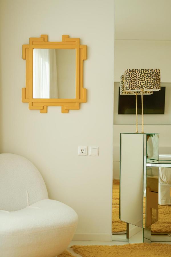 A modern living room corner with a white curved chair, a decorative yellow mirror, and a mirrored console table with a leopard-print lamp—reminiscent of the chic interiors found in the best boutique hotels in Athens.