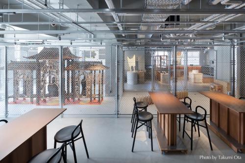 15 Unique Hotels in Tokyo: Coolest hotels 46 A modern, industrial-style room with long wooden tables and black chairs, separated by a wire fence from large, ornate wooden structures—echoing the eclectic design found in unique hotels in Tokyo.