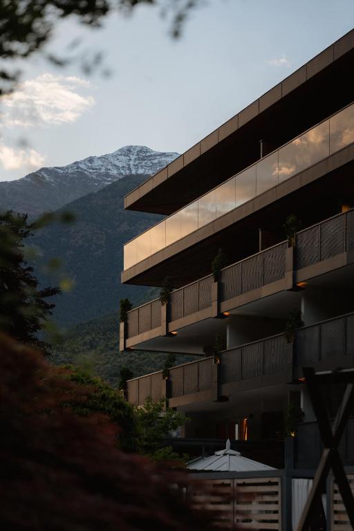 Modern building with glass balconies is seen at sunset, set against a snow-capped mountain and cloudy sky, surrounded by greenery—an ideal retreat among the best hotels in the Dolomites.