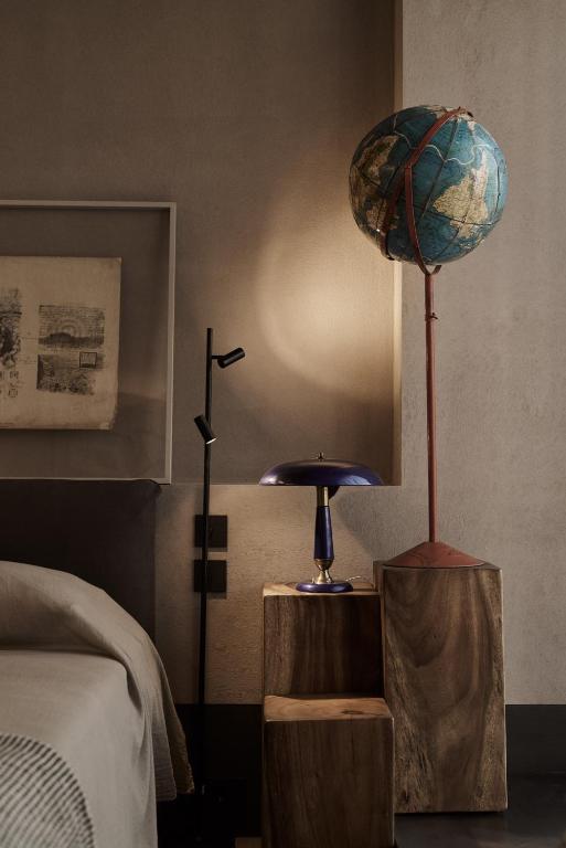A vintage globe lamp and a blue desk lamp illuminate a bedroom setting with a bed and framed artwork, evoking the cozy elegance found in boutique hotels in Athens.