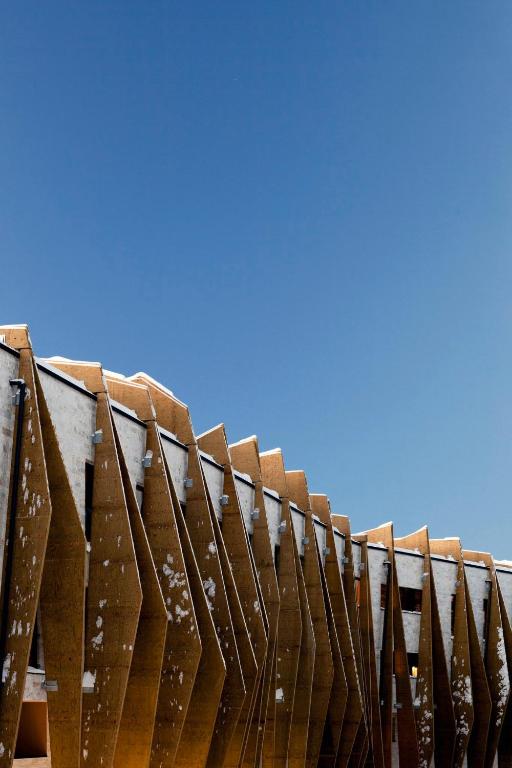 A modern building with large angled wooden panels, partially covered with patches of snow, stands against a clear blue sky—an architectural gem among the best hotels in the Dolomites.