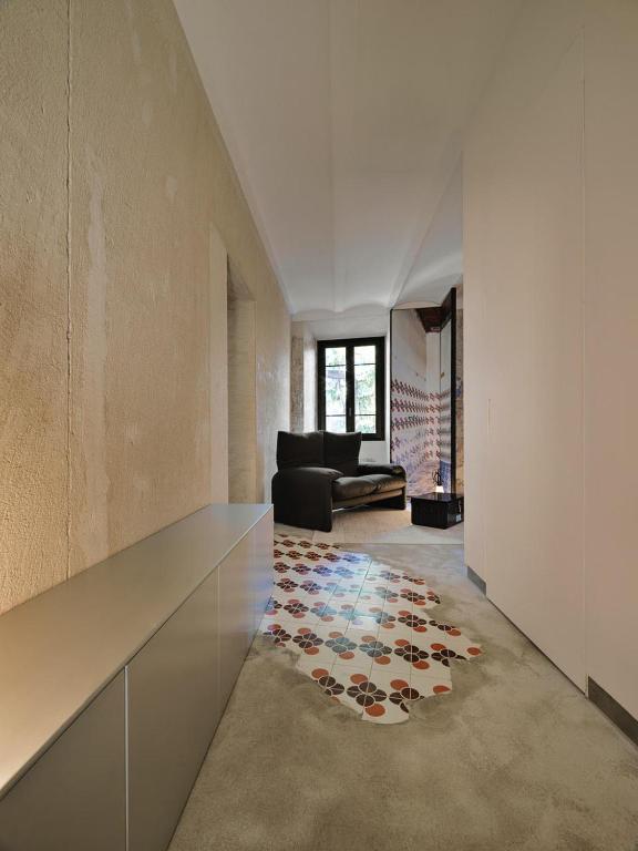 13 UNIQUE Boutique Hotels in Rome 35 A modern hallway with textured beige walls, a sleek metallic cabinet, and decorative floral floor tiles evokes the sophisticated style found in boutique hotels in Rome, leading to a cozy seating area with a black armchair by the window.