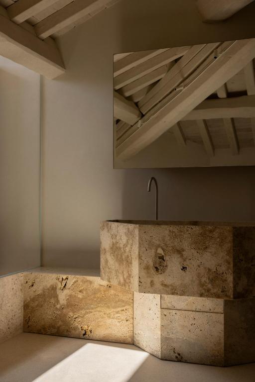 13 UNIQUE Boutique Hotels in Rome 28 A minimalist bathroom with a stone sink and countertop, beige walls, and a large mirror reflecting a wooden beam ceiling—reminiscent of the elegant style found in boutique hotels in Rome. Soft natural light enters from the left.