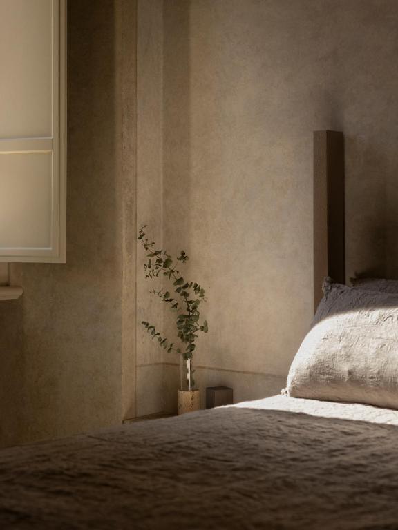 13 UNIQUE Boutique Hotels in Rome 29 A softly lit bedroom corner with a bed covered in beige bedding, a wooden bedpost, and a small vase of greenery on the windowsill, evoking the calm and minimalist atmosphere found in boutique hotels in Rome.