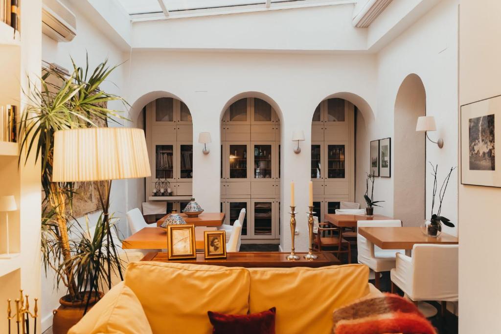 TOP 10 Luxury Hotels in Andalucía 29 Bright, cozy lounge with yellow sofa, framed photos, and candles. Wooden tables with white chairs sit beneath arched doorways. Natural light from a skylight highlights plants—an inviting space inspired by luxury hotels in Andalucía.