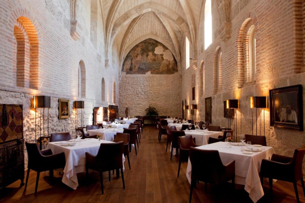 4 Best Hotels in Ribera del Duero, Spain 3 Elegant restaurant with high vaulted stone ceilings, arched windows, and artwork-adorned walls. Perfect for guests from hotels in Ribera del Duero, the refined dining area features white tablecloths and polished wooden floors for a sophisticated experience.