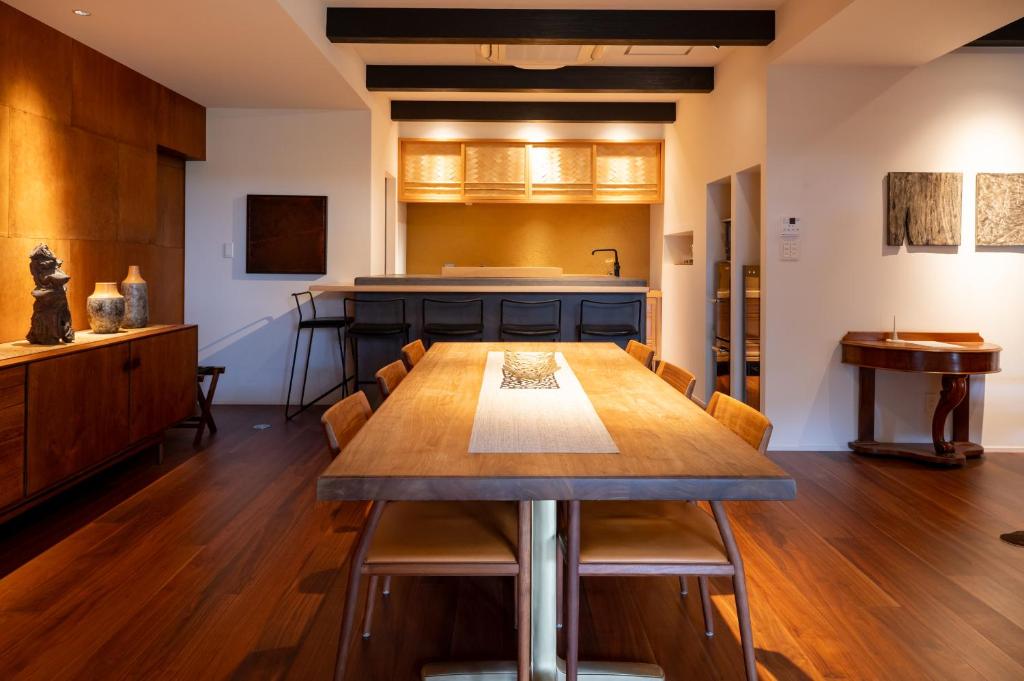 7 Best Hotels in Hiroshima, Japan 24 A modern dining room reminiscent of the best hotels in Hiroshima features a long wooden table with chairs, warm wooden floors, minimalist decor, and an open kitchen area with barstools. Soft lighting creates a cozy atmosphere.