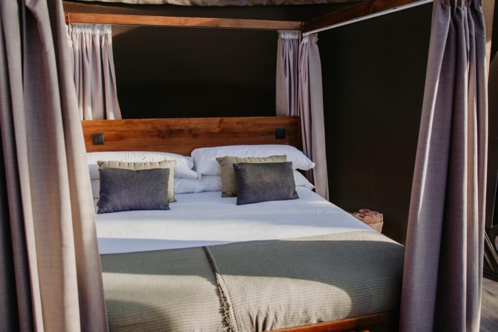 Unique Hotels in Soria: Northern Castile 3 A cozy, neatly made king-sized bed with white sheets and multiple pillows, surrounded by light beige curtains on a wooden four-poster frame, set against dark walls—reminiscent of the elegant suites in hotels in Soria.