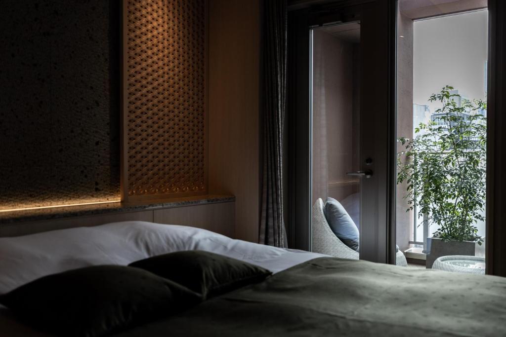 7 Best Hotels in Hiroshima, Japan 26 A cozy bedroom at one of the best hotels in Hiroshima, featuring a dark green bedspread, soft lighting on a textured wall, and a glass door opening to a balcony with a chair and potted plant.