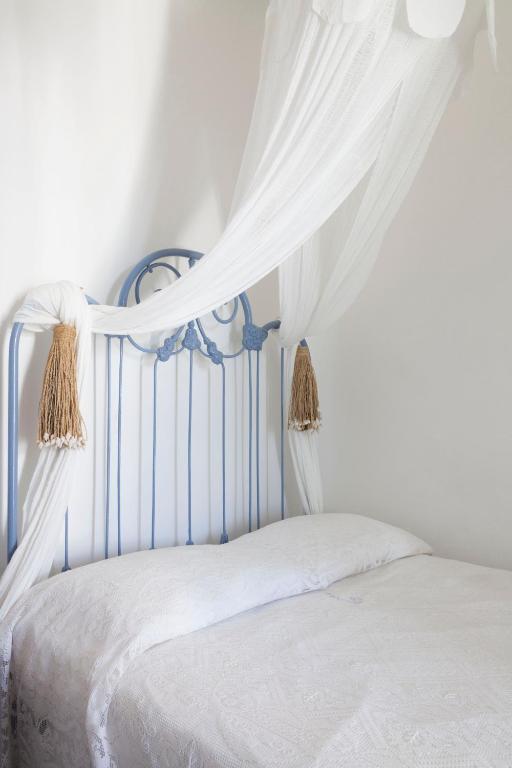 7 Best Hotels in the Aeolian Islands 23 A neatly made bed with a light blue metal headboard and white bedding evokes the tranquil charm of hotels in the Aeolian Islands. A sheer white canopy with gold tassels adds a soft, airy touch to the bright, white-walled room.