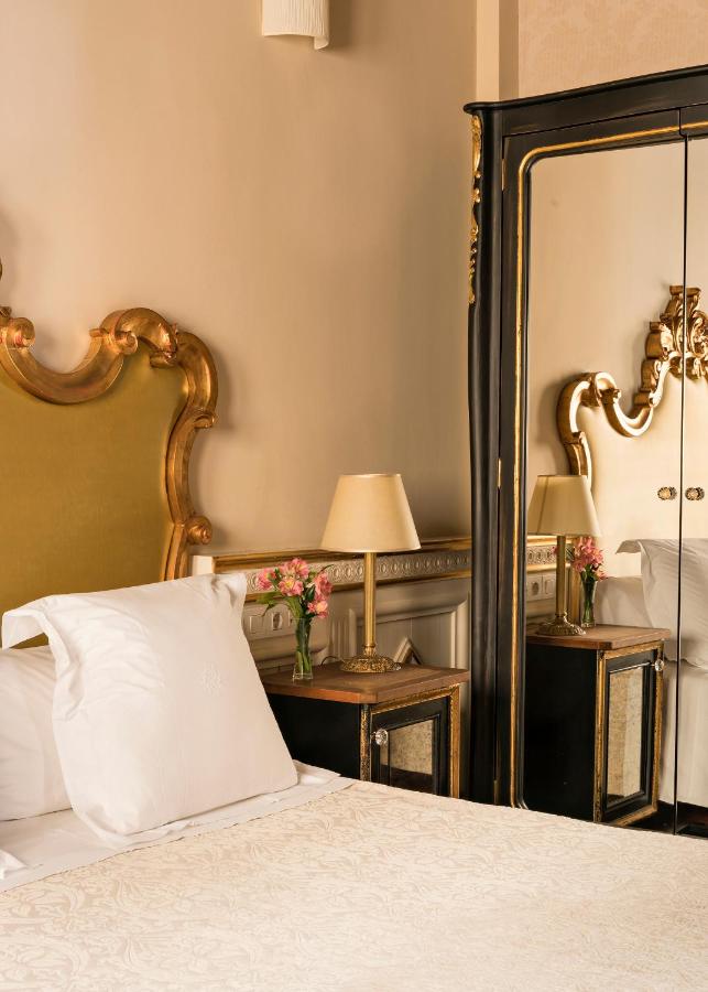 Elegant bedroom with a green and gold upholstered headboard, white bedding, and a mirrored wardrobe—this space echoes the refined charm of boutique hotels in Granada, complete with ornate decor and fresh pink flowers by the bedside.