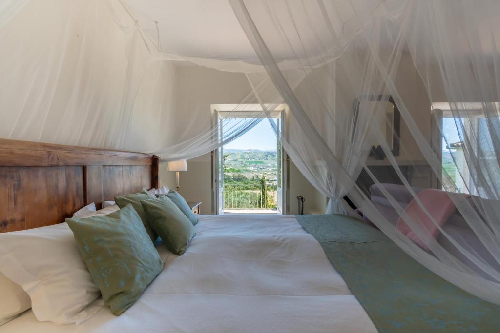 TOP 10 Luxury Hotels in Andalucía 40 A cozy bedroom with a wooden headboard, pillows, and a green bedspread beneath a white canopy—reminiscent of luxury hotels in Andalucía. Two windows reveal scenic greenery and hills, as natural light fills the inviting space.