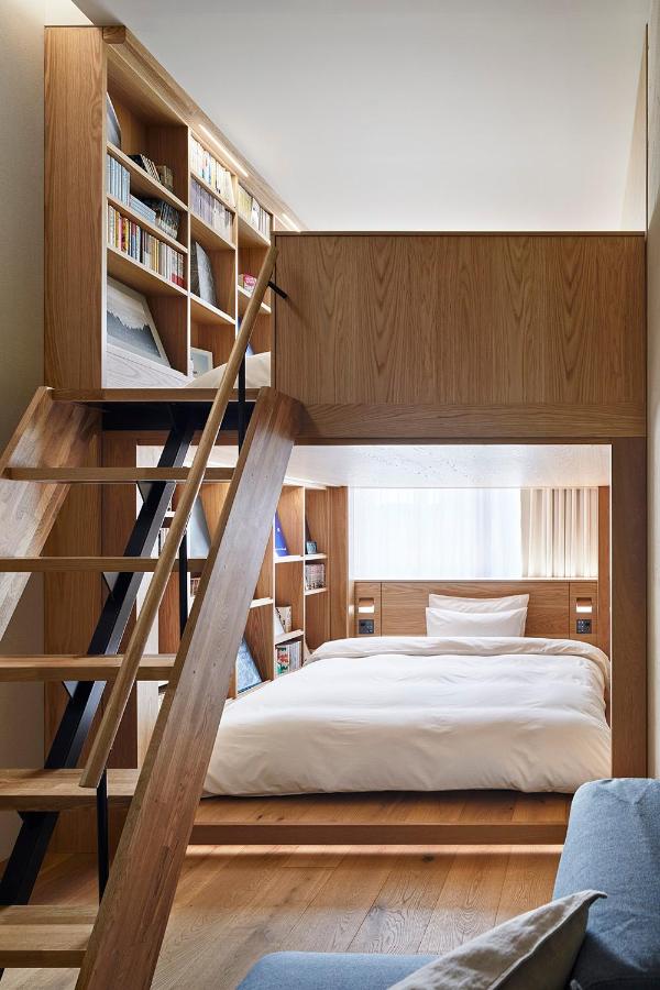 15 Unique Hotels in Tokyo: Coolest hotels 22 A modern loft bedroom with wooden floors, a lower double bed surrounded by built-in bookshelves, and an upper level accessed by a wooden staircase lined with bookshelves—reminiscent of the cozy style found in unique hotels in Tokyo.