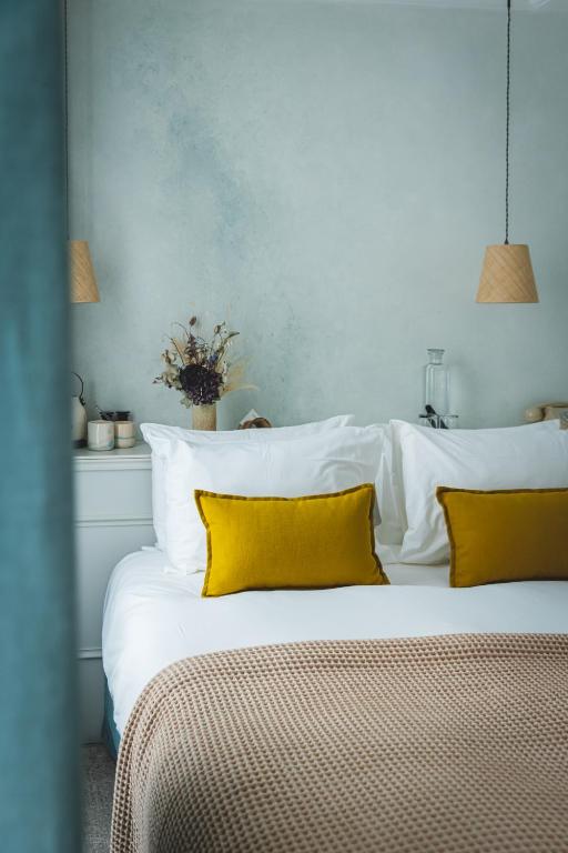 13 Unique Hotels in Paris for a Stylish Stay 29 Modern bedroom reminiscent of unique hotels in Paris, with a neatly made bed featuring white linens, mustard yellow pillows, a beige textured blanket, and bedside tables adorned with dried flowers and lamps against a light blue wall.
