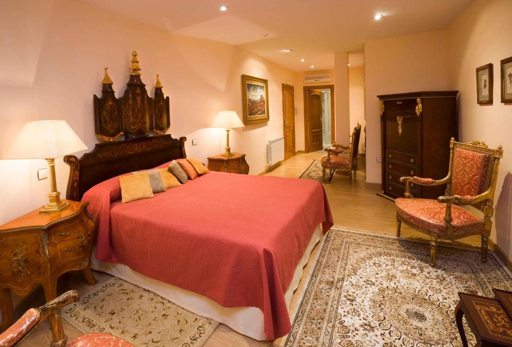 4 Best Hotels in Ribera del Duero, Spain 23 Elegant bedroom with a large bed covered in a red bedspread, ornate wooden furniture, antique chairs, rugs, and warm lighting—evoking the classic, luxurious ambiance found in many boutique hotels in Ribera del Duero.