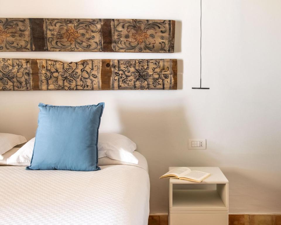 7 Best Hotels in the Aeolian Islands 16 A neatly made bed with a blue pillow sits next to a white nightstand holding an open book, reminiscent of stylish hotels in the Aeolian Islands. Decorated wooden panels hang above, and a modern hanging lamp is visible.