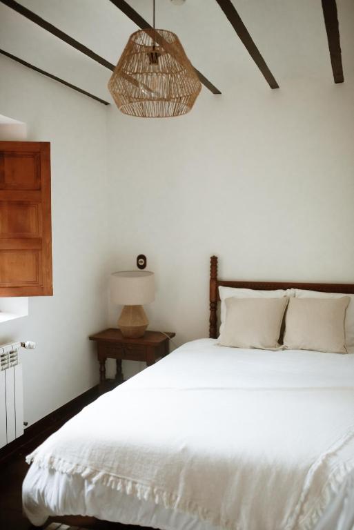 A cozy bedroom reminiscent of boutique hotels in Cantabria, featuring a wooden bed, white bedding, two beige pillows, a wooden nightstand with a lamp, an open wooden window, and a woven pendant light on the ceiling.