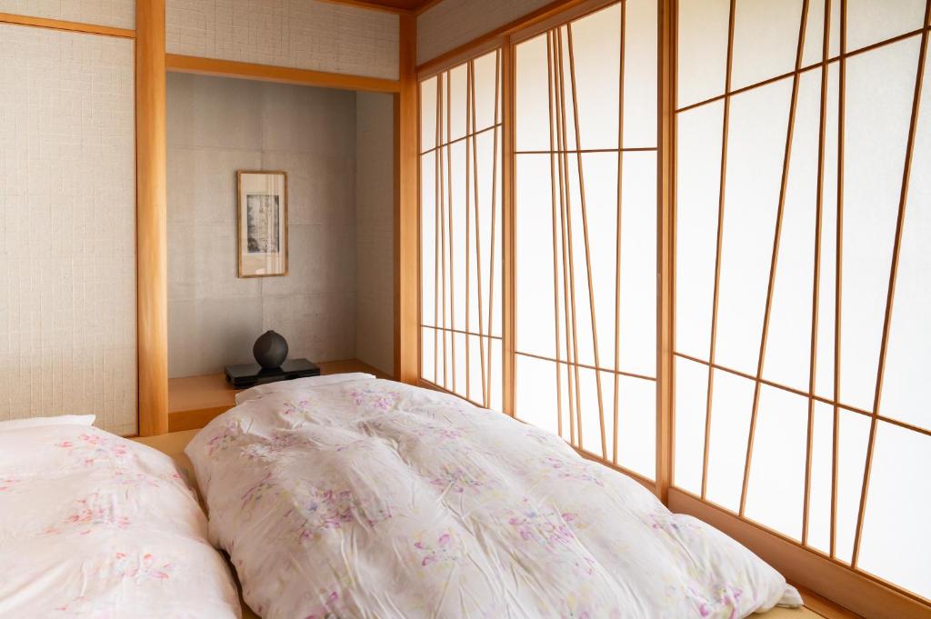 7 Best Hotels in Hiroshima, Japan 23 A serene Japanese-style bedroom reminiscent of the best hotels in Hiroshima, with two futons covered in floral duvets, soft natural light streaming through traditional shoji screens, and minimalist decor featuring a framed artwork and a small sculpture.