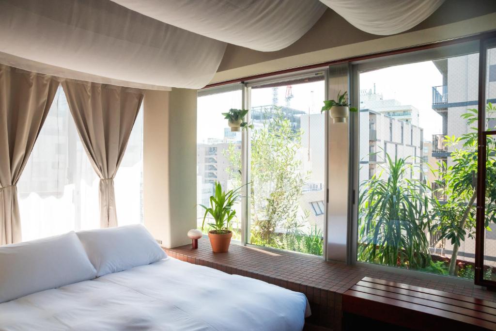 15 Unique Hotels in Tokyo: Coolest hotels 39 A bright bedroom in one of the unique hotels in Tokyo, featuring large windows, sheer curtains, a white bed, and green potted plants on a tiled ledge overlooking city buildings outside.