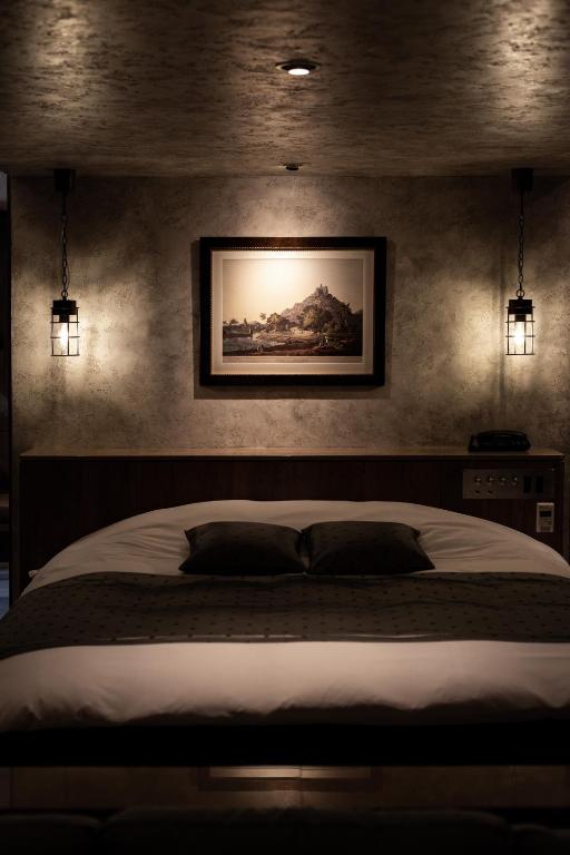 7 Best Hotels in Hiroshima, Japan 28 A cozy, dimly lit bedroom inspired by the best hotels in Hiroshima, featuring a double bed with two pillows, hanging lantern-style lights on either side, and a framed picture of a mountain above the headboard.