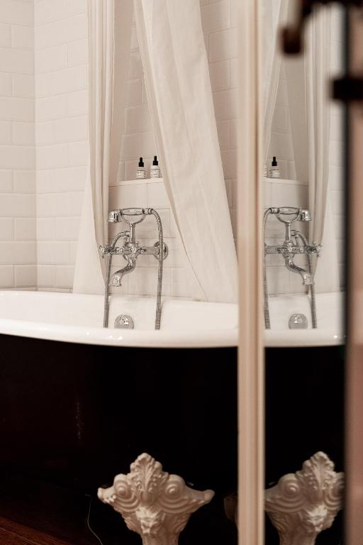 13 Unique Hotels in Paris for a Stylish Stay 52 A vintage-style bathtub with ornate claw feet stands in front of white tiled walls, partially enclosed by a white shower curtain—evoking the timeless elegance found in unique hotels in Paris. Two bottles are placed on the tub’s rim.