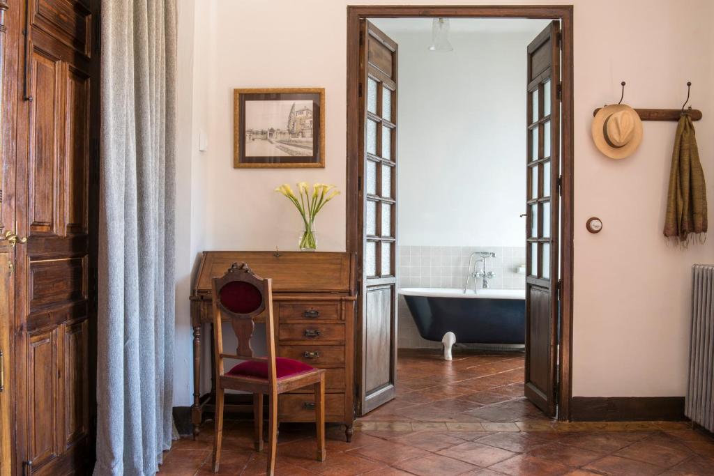 TOP 10 Luxury Hotels in Andalucía 32 A vintage room inspired by luxury hotels in Andalucía, with a wooden desk and red chair, a framed picture on the wall, and yellow flowers in a vase. Through double doors is a bathroom with a black clawfoot tub; a hat and scarf hang on the hook.