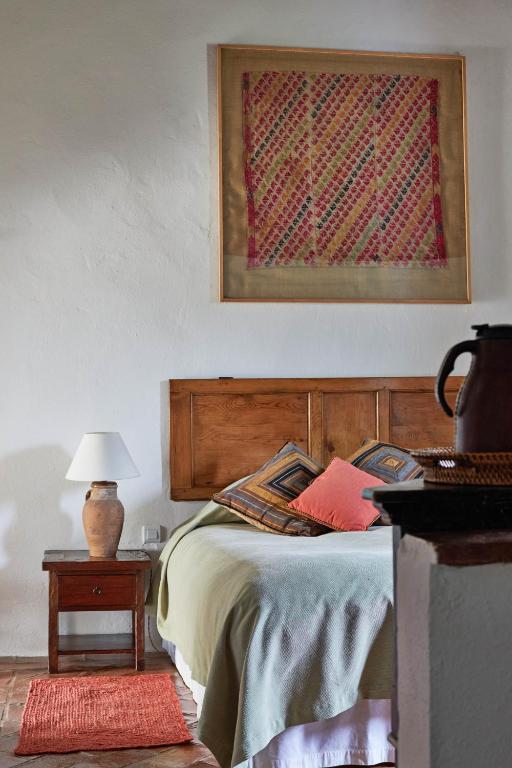 TOP 10 Luxury Hotels in Andalucía 14 Cozy bedroom with a wooden headboard, colorful throw pillows, a green blanket, and a bedside table with a lamp and terracotta vase—reminiscent of the inviting style found in luxury hotels in Andalucía. Framed textile art hangs above the bed.