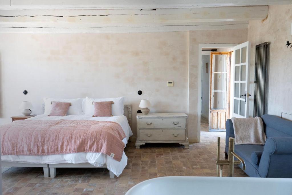 TOP 10 Luxury Hotels in Andalucía 10 A cozy bedroom reminiscent of luxury hotels in Andalucía, featuring a large bed with white and pink bedding, a light gray dresser, blue sofa, and rustic tile flooring. Sunlight pours through an open door, creating a bright and airy ambiance.