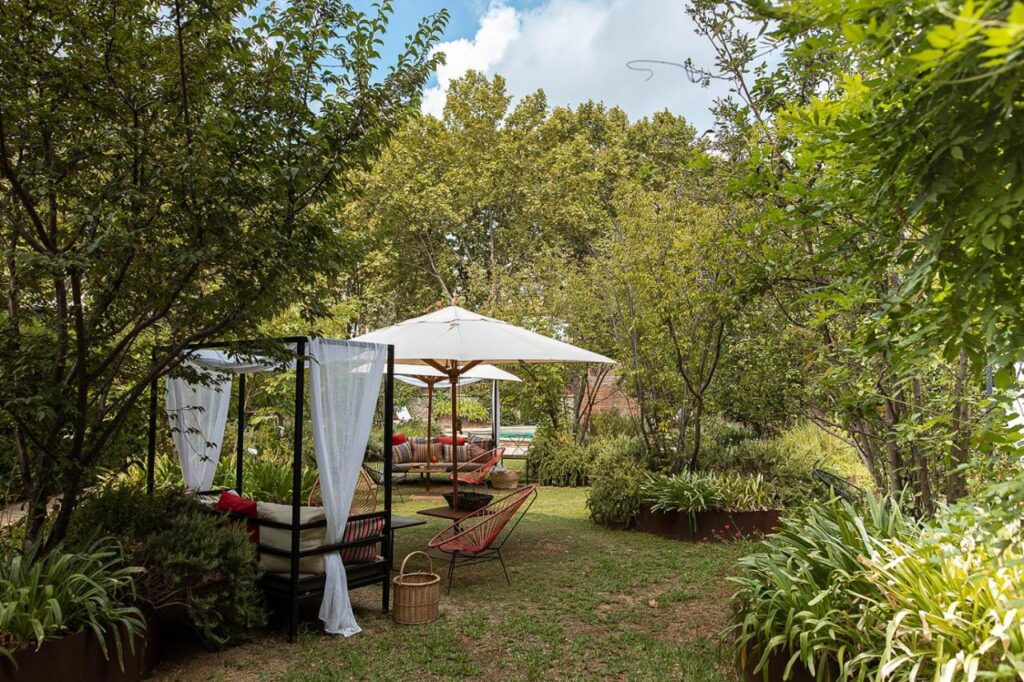 13 Unique Hotels in Barcelona, Spain 10 A lush garden with trees and greenery features outdoor seating under a white canopy and transparent drapes, with lounge chairs and a small table—creating a relaxing, shaded retreat reminiscent of unique hotels in Barcelona.