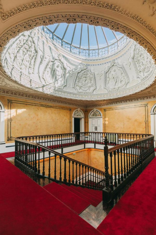 Top 12 Boutique Hotels in Porto, Portugal 11 Large ornate room with a detailed white domed ceiling and skylight, featuring classical sculptures—a striking space reminiscent of the elegance found in boutique hotels in Porto, with yellow walls, red carpet, and a dark wooden railing around a central staircase.