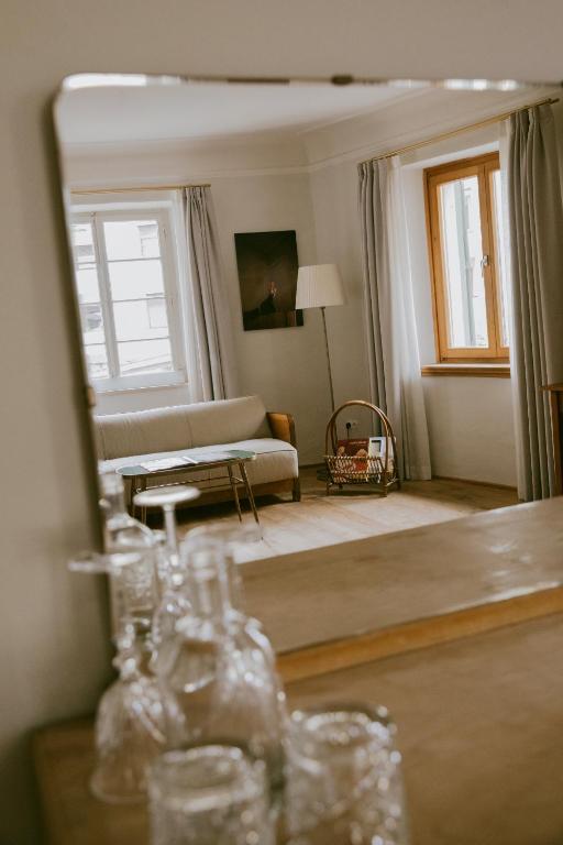 Reflection of a cozy living room in a mirror, reminiscent of the inviting lounges found in the best hotels in the Dolomites; a sofa, floor lamp, side table, and soft curtains create a warm scene with blurred glassware in the foreground.