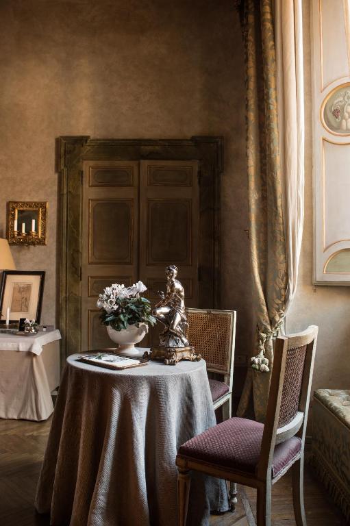 13 UNIQUE Boutique Hotels in Rome 47 A small round table with a gray tablecloth, a flower arrangement, and a statue sits between two chairs in an elegant, softly lit room with tall curtains and classic wooden doors—reminiscent of boutique hotels in Rome.