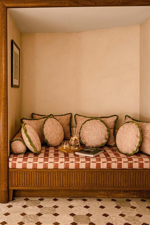 13 Unique Hotels in Paris for a Stylish Stay 36 Cozy alcove in one of the unique hotels in Paris, featuring a wooden built-in daybed, checkered red and beige cushion, round pink pillows with green trim, and a tray with teapot and cups. Framed art above, patterned tile floor below.