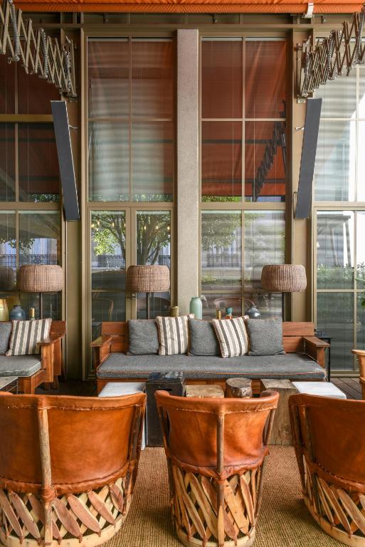 13 Unique Hotels in Paris for a Stylish Stay 47 A cozy lounge area, reminiscent of unique hotels in Paris, features brown leather chairs, a wooden coffee table, and a cushioned sofa with striped pillows. Large windows behind reveal greenery and fill the space with natural light.