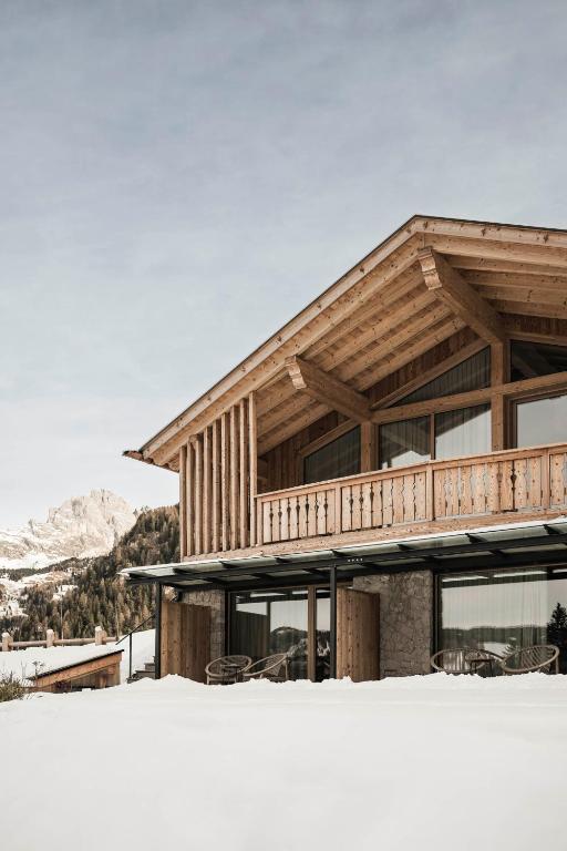A modern wooden chalet with large windows and a balcony sits in a snowy landscape, offering mountain views—an inviting retreat reminiscent of the best hotels in the Dolomites.