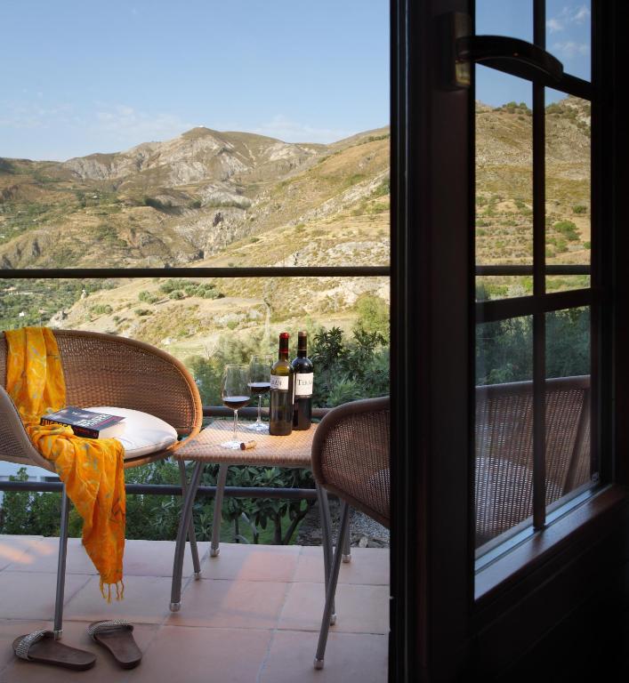 TOP 10 Luxury Hotels in Andalucía 26 A cozy balcony with two wicker chairs, a small table with wine, glasses, and a book overlooks scenic mountains—echoing the charm of luxury hotels in Andalucía. A yellow scarf and sandals add a relaxed atmosphere next to an open door.