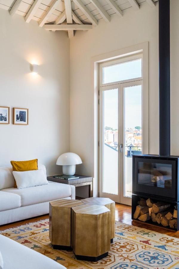 Top 12 Boutique Hotels in Porto, Portugal 38 Bright, modern living room with a white sofa, yellow pillow, geometric brass tables, and a black wood stove—reminiscent of the chic interiors found in boutique hotels in Porto. Glass doors lead to a balcony; wall art and beamed ceiling add charm.