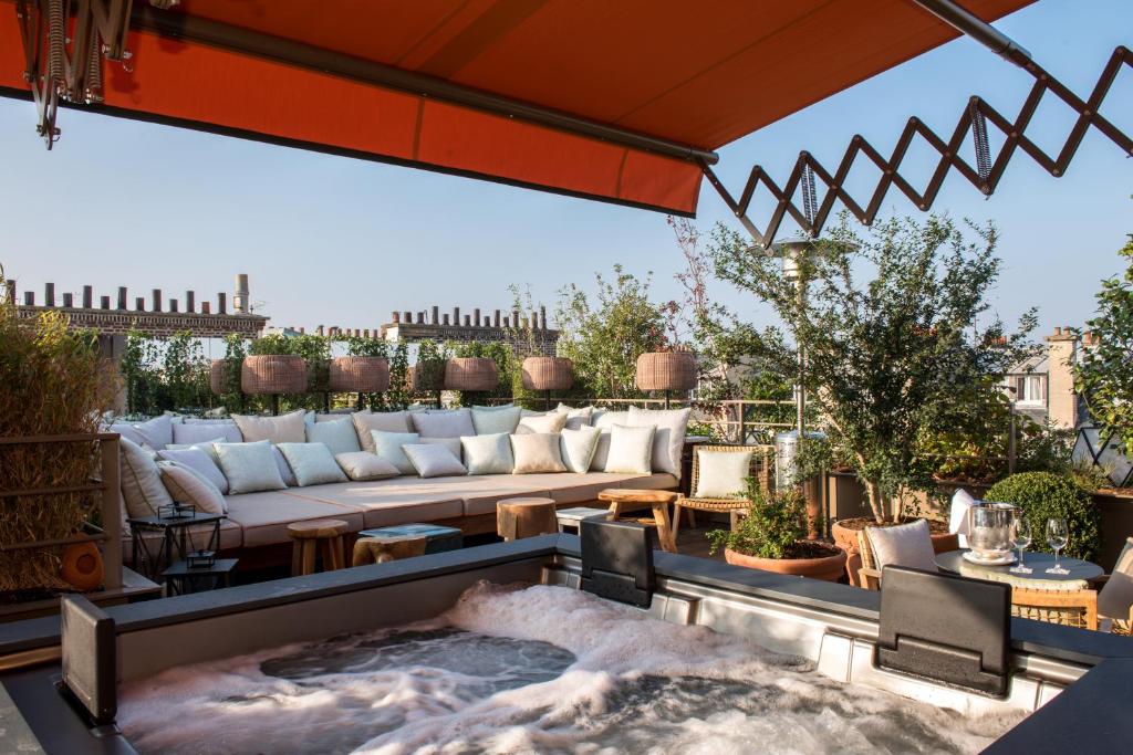 13 Unique Hotels in Paris for a Stylish Stay 48 A rooftop terrace at one of the unique hotels in Paris, featuring a large cushioned seating area, potted plants, wicker lanterns, and a bubbling hot tub under an orange retractable awning with a clear blue sky overhead.
