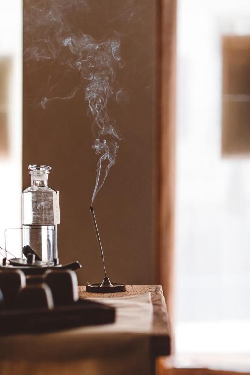 13 Unique Hotels in Paris for a Stylish Stay 32 A stick of incense emits curling smoke next to a glass bottle and cup on a wooden table, with soft, natural light streaming through a blurred window—evoking the tranquil ambiance of unique hotels in Paris.